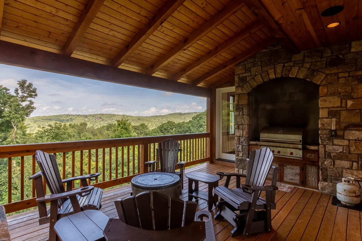 An outdoor deck with comfortable seating, a stone grill, and panoramic views of the surrounding hills and forests. The scene suggests an ideal spot for barbecues, sunset cocktails, or simply soaking in the mountain atmosphere, extending the communal experience outdoors.