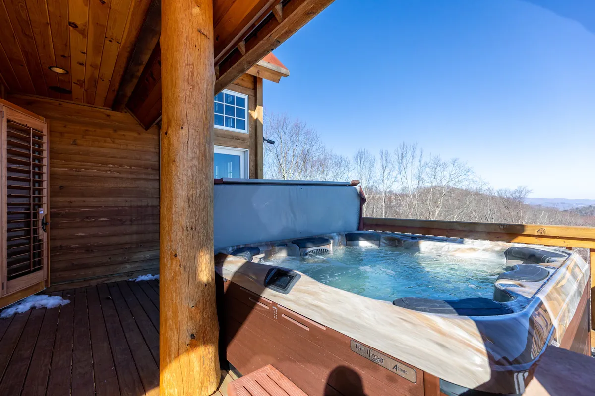 A tranquil hot tub set beneath rustic wooden beams with a breathtaking view of the Blue Ridge Mountains in the background. The outdoor setting blends relaxation with natural beauty.