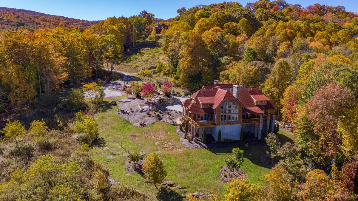 The hero image showcases a spacious, luxurious house with a striking red roof, nestled amidst a vibrant tapestry of colorful trees. A winding driveway leads up to the home, set against a stunning natural backdrop that hints at privacy, tranquility, and sweeping mountain views.