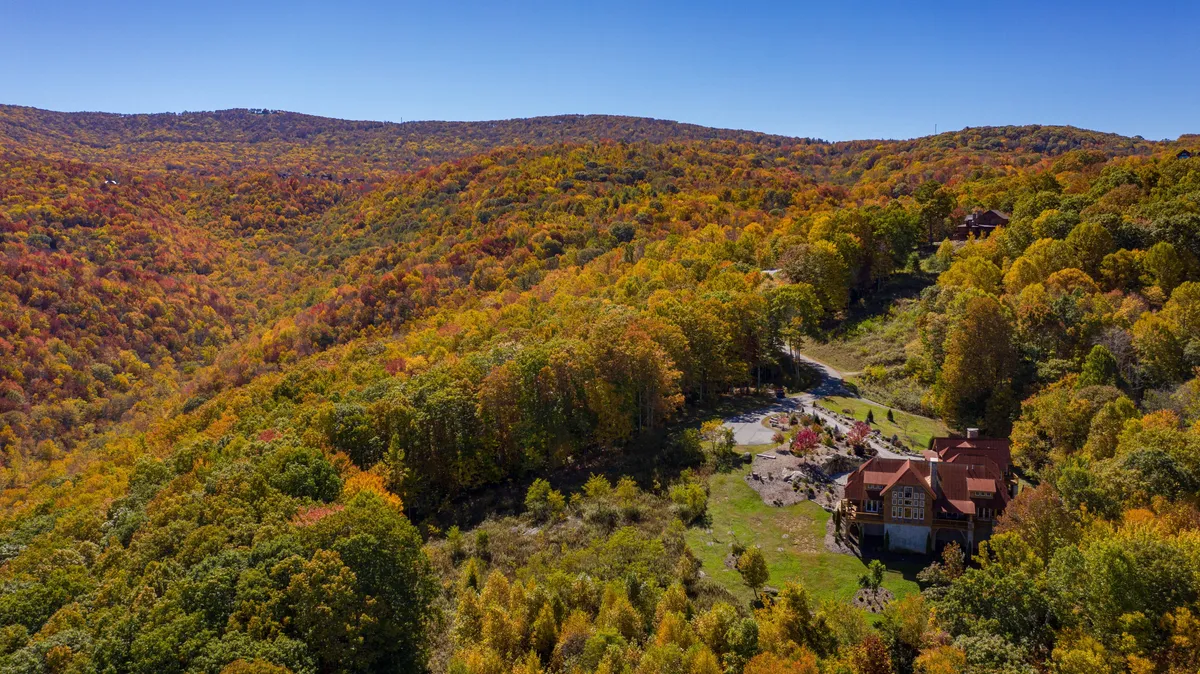 An exterior view of the house set against a backdrop of surrounding mountains and vibrant fall foliage. The scene is serene, highlighting the natural beauty and tranquility of the area.