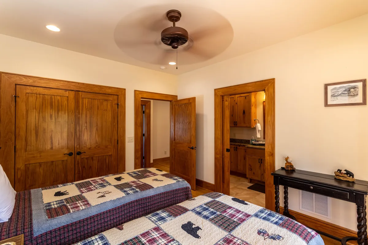 A twin bedroom featuring two beds with patterned quilts, warm wooden doors and ceiling fan, and a small table with decorative touches. The room is comfortable and homely, perfect for friends or kids traveling together.