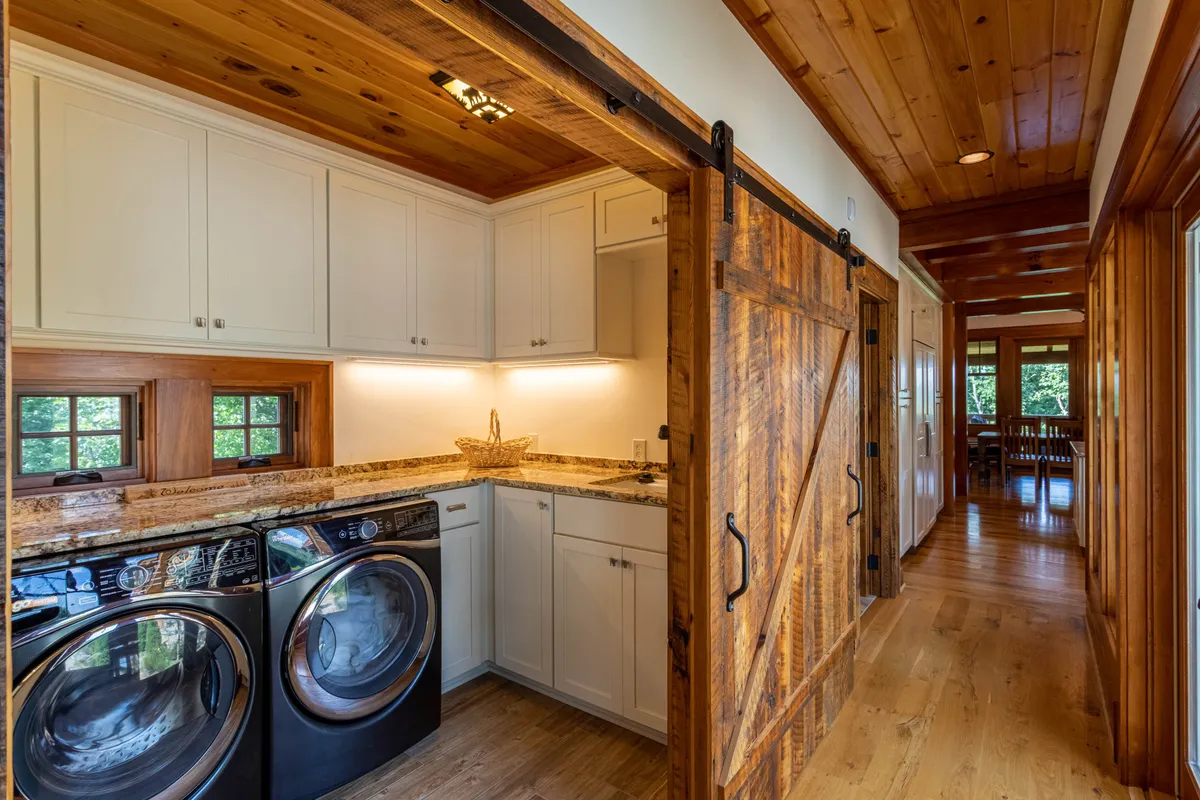 A functional laundry/mud room with a washing machine, granite countertop, and a rustic wooden barn door, filled with natural light. The space is both practical and inviting, supporting longer or independent stays.