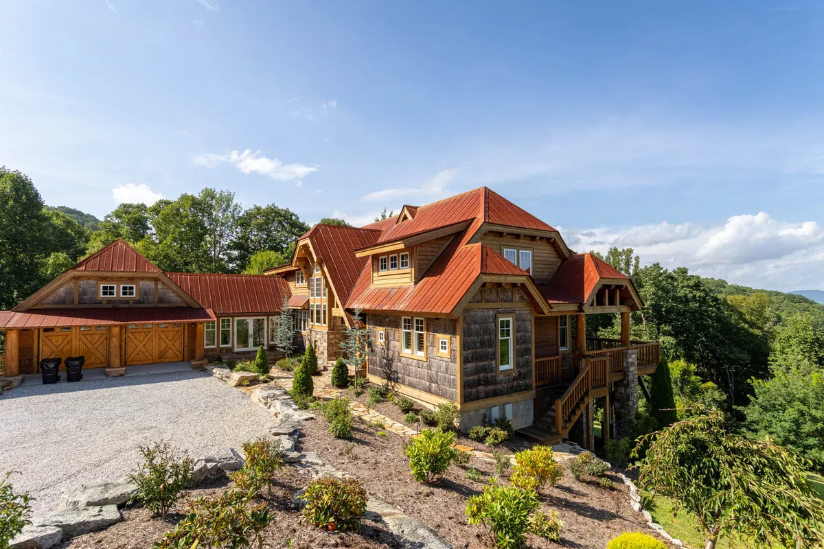 A wide exterior shot featuring the home’s unique architecture with a vibrant red roof, surrounded by landscaped gardens and set against a backdrop of mountains. The scene includes inviting outdoor spaces ideal for group gatherings and enjoying nature.