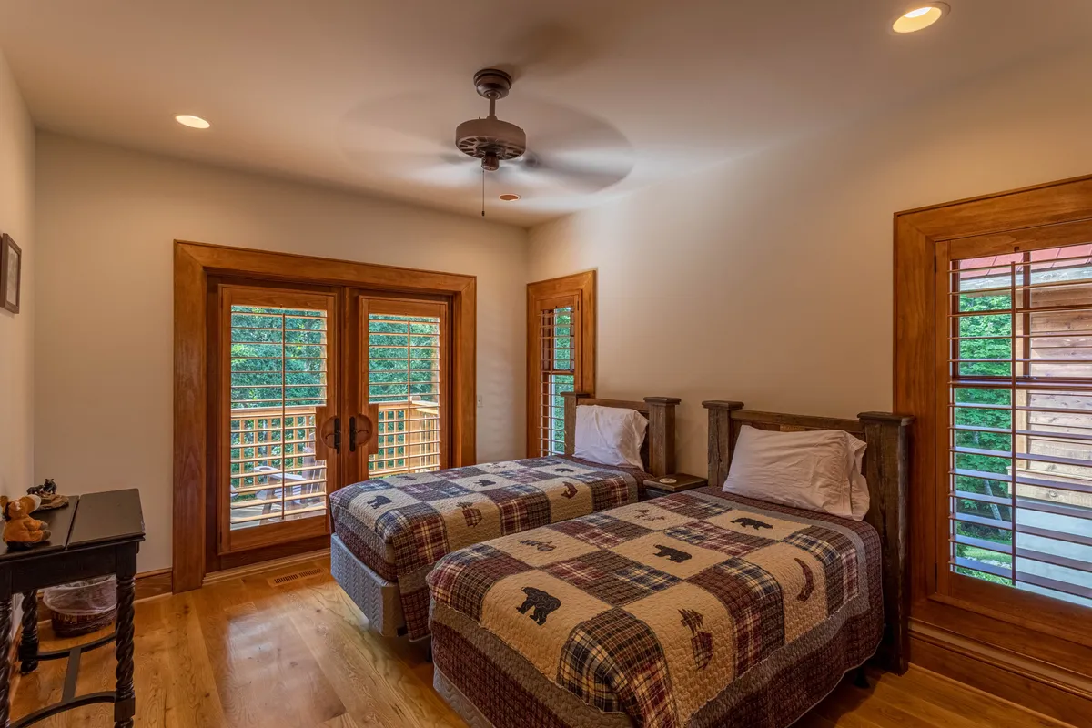A bright and airy twin bedroom with matching patterned quilts, wooden window frames, and a ceiling fan overhead. The inviting décor and natural light make it suitable for guests of all ages seeking comfort and privacy.