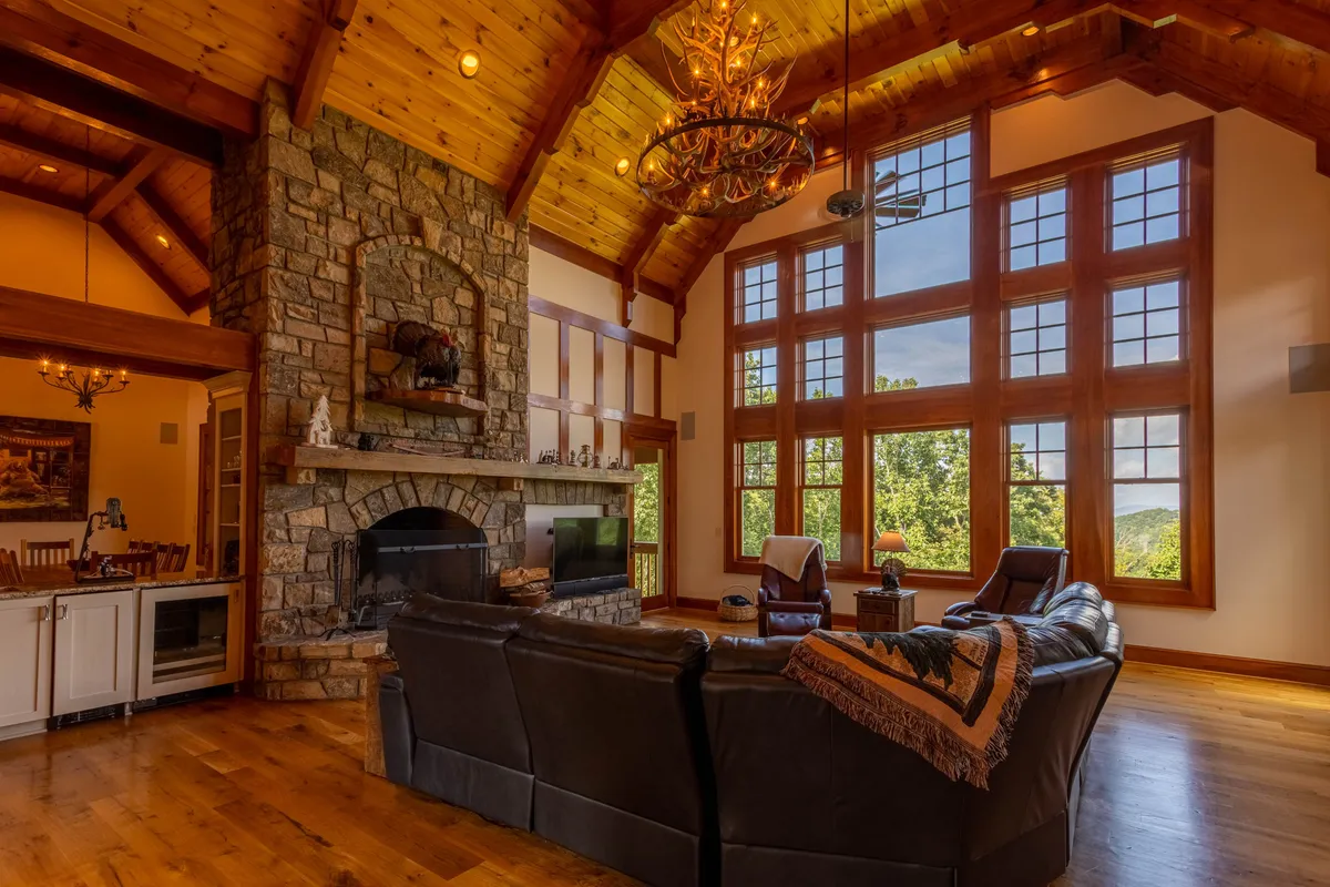 A cozy open-concept living area with a prominent stone fireplace, large windows that flood the room with natural light, a classic chandelier, and comfortable seating. The atmosphere is both intimate and spacious, ideal for relaxing or socializing.