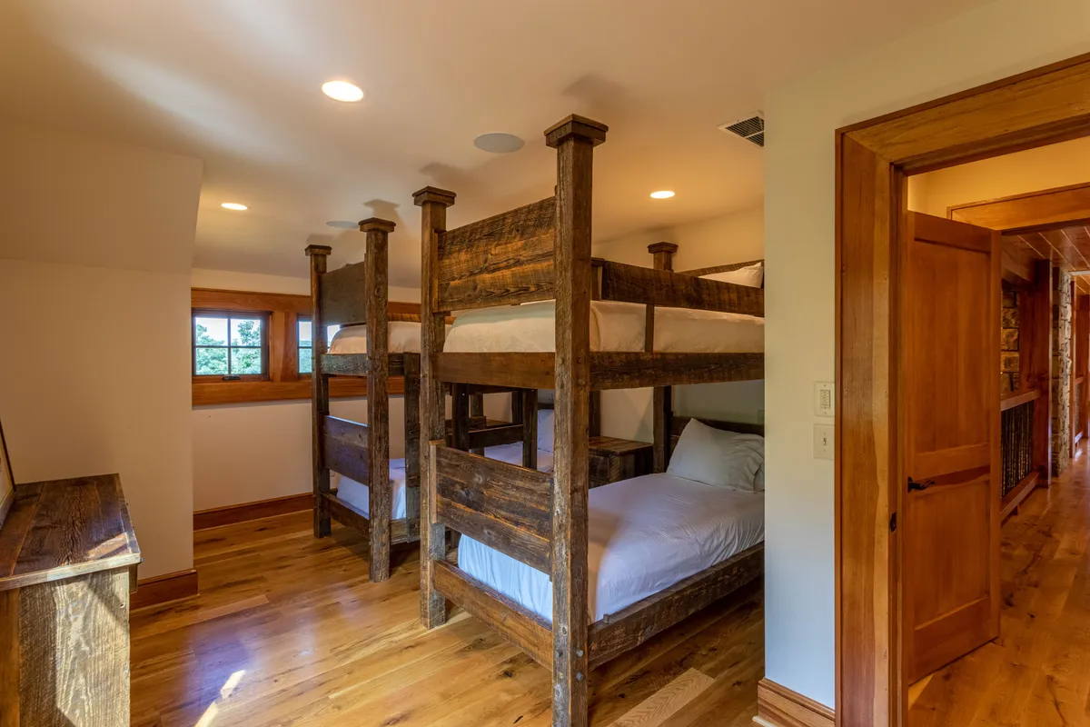 A playful bunk room designed for children or teens, with sturdy wooden bunk beds and windows that let in natural light. The space exudes a sense of comfort and togetherness, ideal for group stays and family fun.